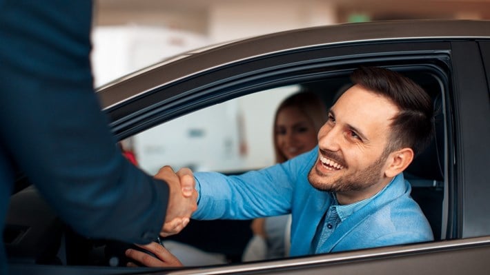 Smilende par i nykjøpt bil takker bilselger med håndtrykk