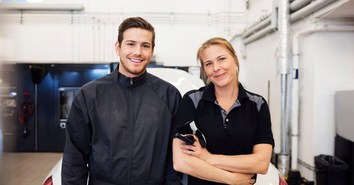 ung mannlig og kvinnelig mekaniker smiler på verksted