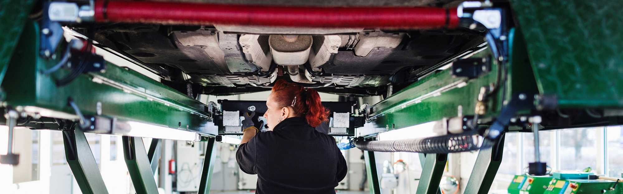 ung kvinnelig mekaniker inspiserer bilens understell
